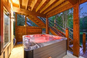 A hot tub in a wooden deck area with a wooden staircase and a wooden fence in the background.