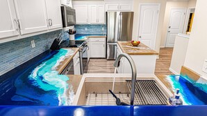 Uma cozinha com armários brancos, geladeira de aço inoxidável, painel de azulejos azul e uma pia com padrão de ondas.