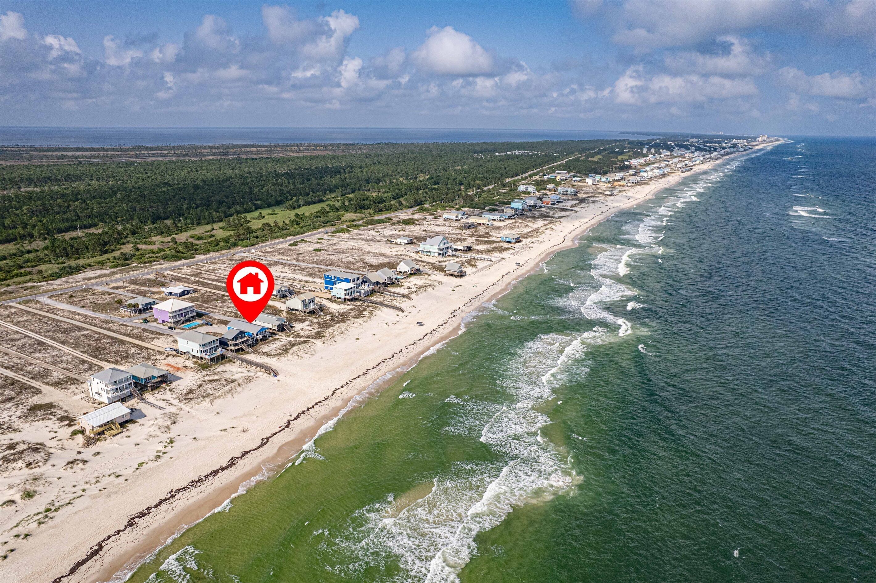 An aerial view of a coastal area with a beach, houses, and a large body of water.