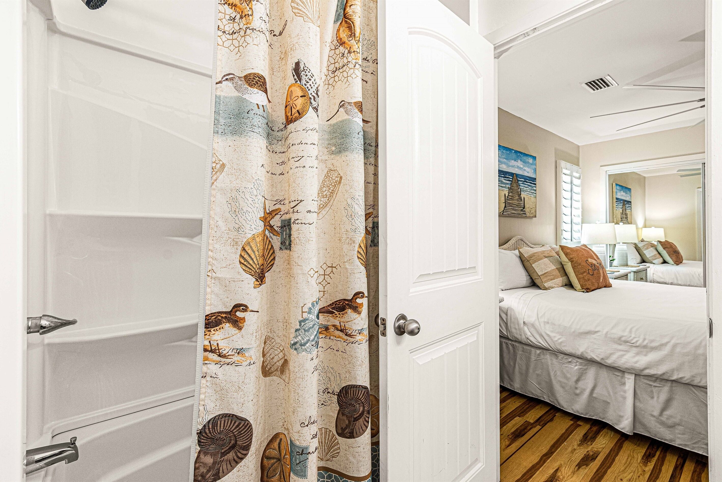 A hotel room with a large bed, a bathroom with a bathtub, and a curtain with bird and shell patterns.