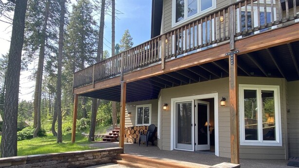 A two-story house with a covered patio, stone fire pit, and a deck with a railing. - Gt254 Goat Trail Lookout (Whitefish)