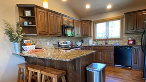 A kitchen with wooden cabinets, a granite countertop, a stainless steel trash can, and a window providing natural light. - Gt254 Goat Trail Lookout (Whitefish)