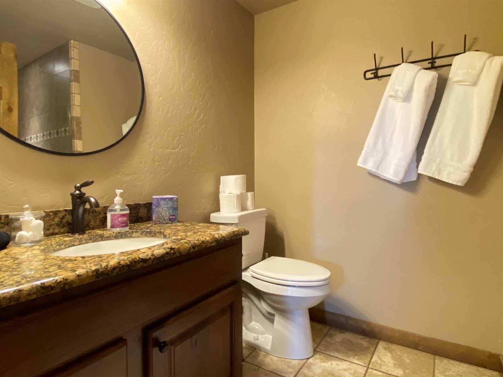 A bathroom with a granite countertop, a sink, a mirror, a toilet, and a towel rack with two towels.