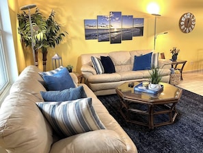 A living room with a beige sofa, a coffee table, and a wall-mounted clock.
