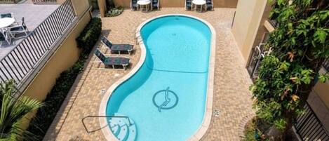 A swimming pool with lounge chairs and a lifeguard chair, surrounded by a brick patio and a fence.