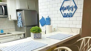 A kitchen with white cabinets, a stainless steel refrigerator, a microwave, and a sign reading 'Mumosa BAR'. - Beachfront Paradise w/ King Room, Pool, Hot Tub! (South Padre Island)