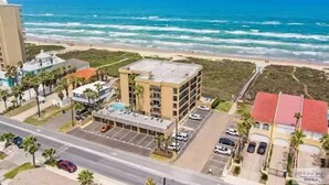 An aerial view of a coastal building with a parking lot and a beach in the background. - Beachfront Paradise w/ King Room, Pool, Hot Tub! (South Padre Island)