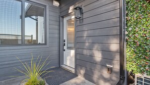 A house with a gray exterior, a white door, and a small garden area with a plant and a doormat. - PRIVATE Hot Tub with Valley Views!! (Colwood)