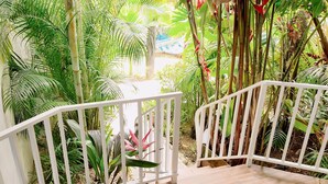 A wooden deck with a white railing, surrounded by lush greenery and plants. - Arenal Poshpacker Boutique Urban Tropical Hotel (La Fortuna)