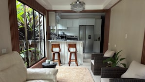 A modern living room with a sofa, a coffee table, and a view of a kitchen and dining area. - Arenal Poshpacker Boutique Urban Tropical Hotel (La Fortuna)