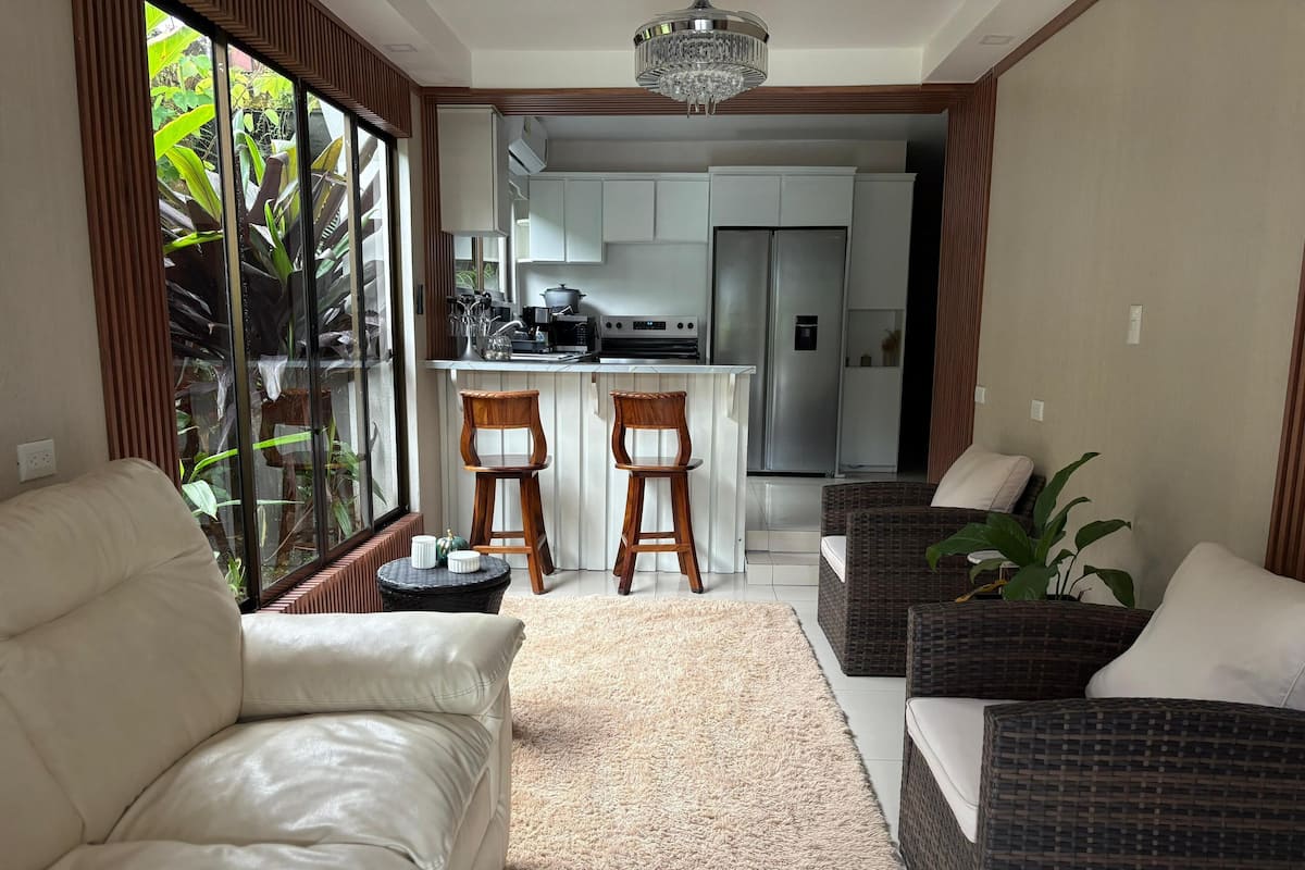 A modern living room with a sofa, a coffee table, and a view of a kitchen and dining area.