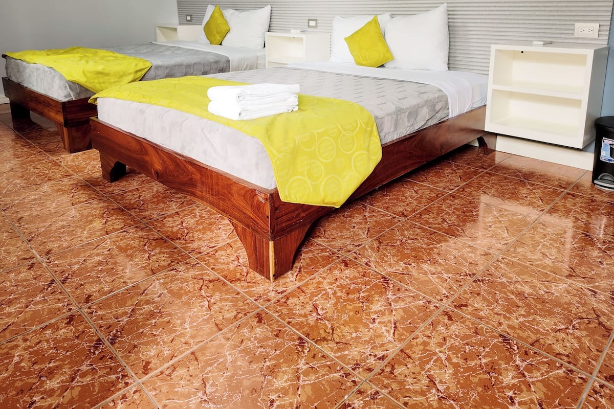 A hotel room with two beds, a wooden headboard, a marble floor, and a white nightstand.
