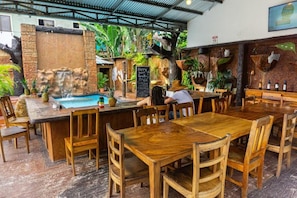 Un restaurant avec des tables et des chaises en bois, une cascade décorative et des plantes tropicales.