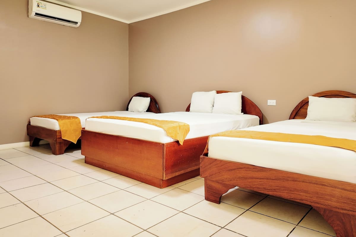 A hotel room with three wooden beds, a tiled floor, and an air conditioning unit on the wall.
