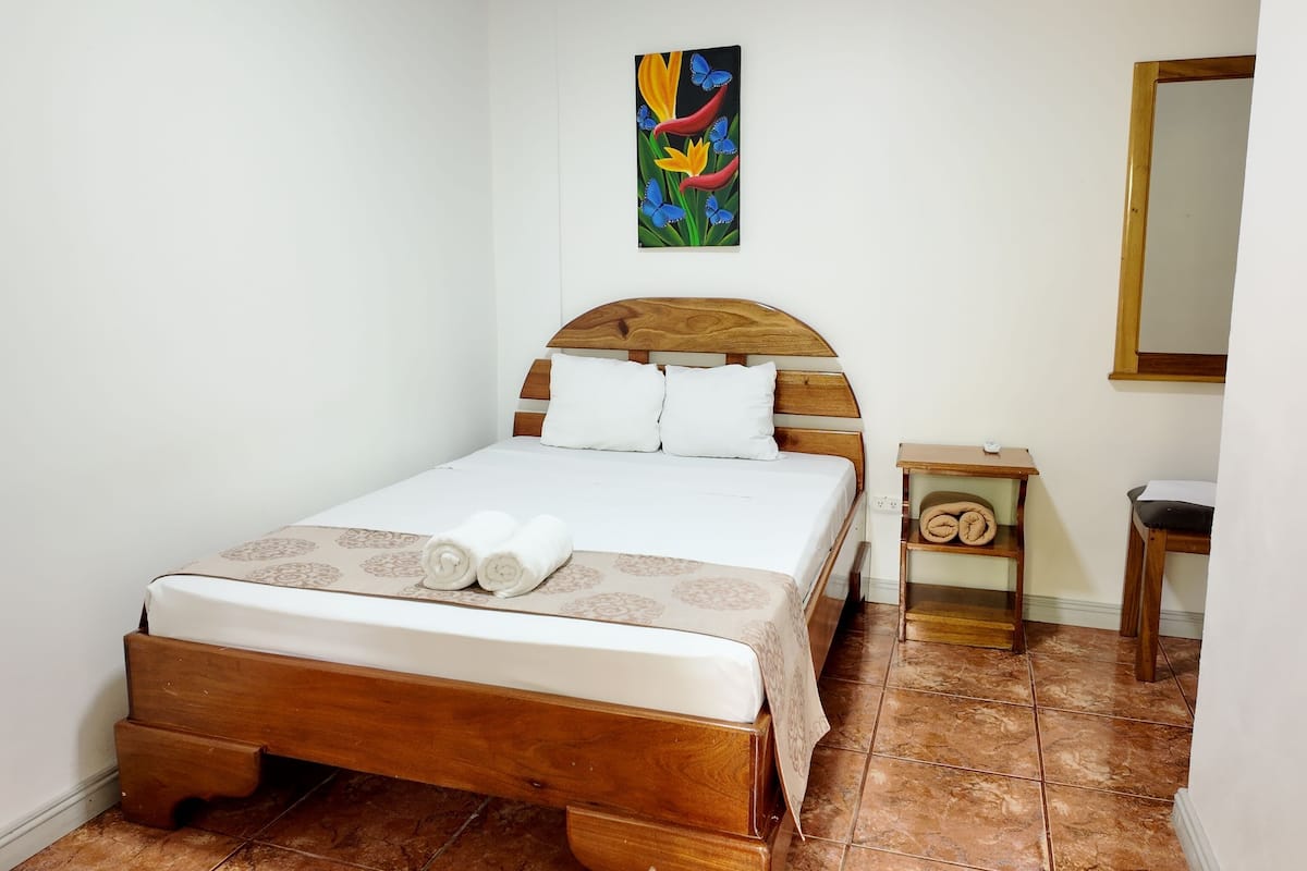 A neatly made bed with a wooden headboard, a small bedside table with a lamp, and a colorful painting on the wall.