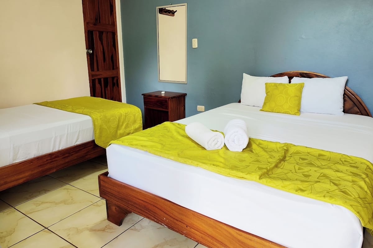 A hotel room with two beds, a wooden wardrobe, a small bedside table, and a mirror on the wall.