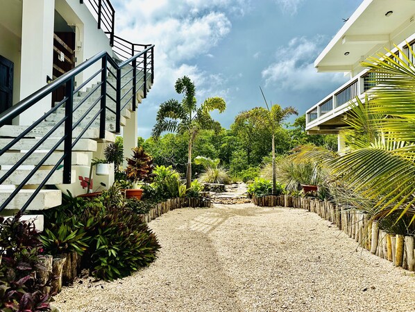 A modern building with a staircase leading to a balcony, surrounded by a gravel pathway and lush greenery. - Charming Modern Beach Villa with 360 Island views & easy resort access (San Pedro)