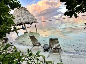 A beach with two wooden lounge chairs and a thatched-roof structure. - Charming Modern Beach Villa with 360 Island views & easy resort access (San Pedro)