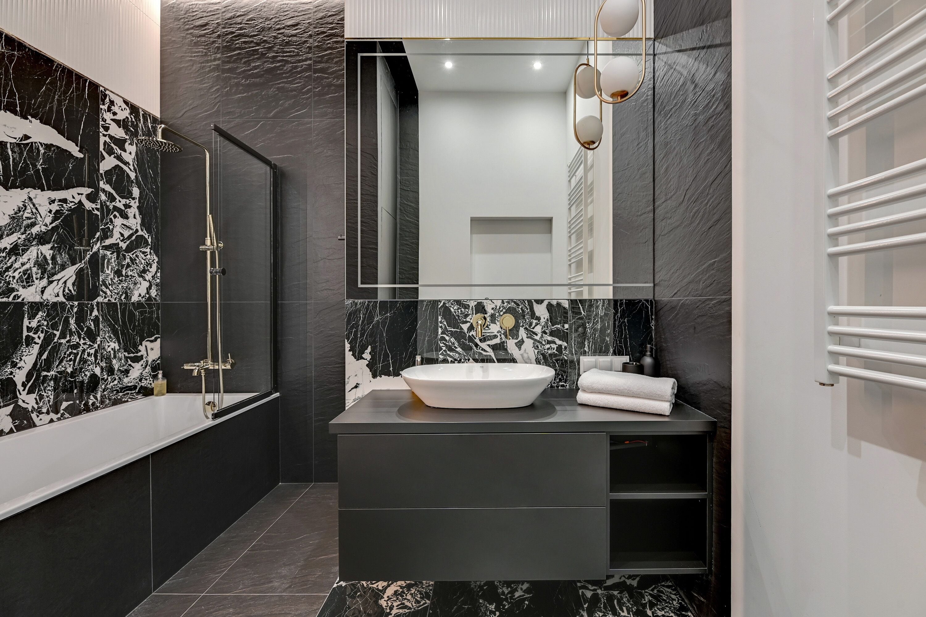 Un baño moderno con tocador de mármol blanco y negro, un espejo grande y una zona de ducha con mampara de vidrio.