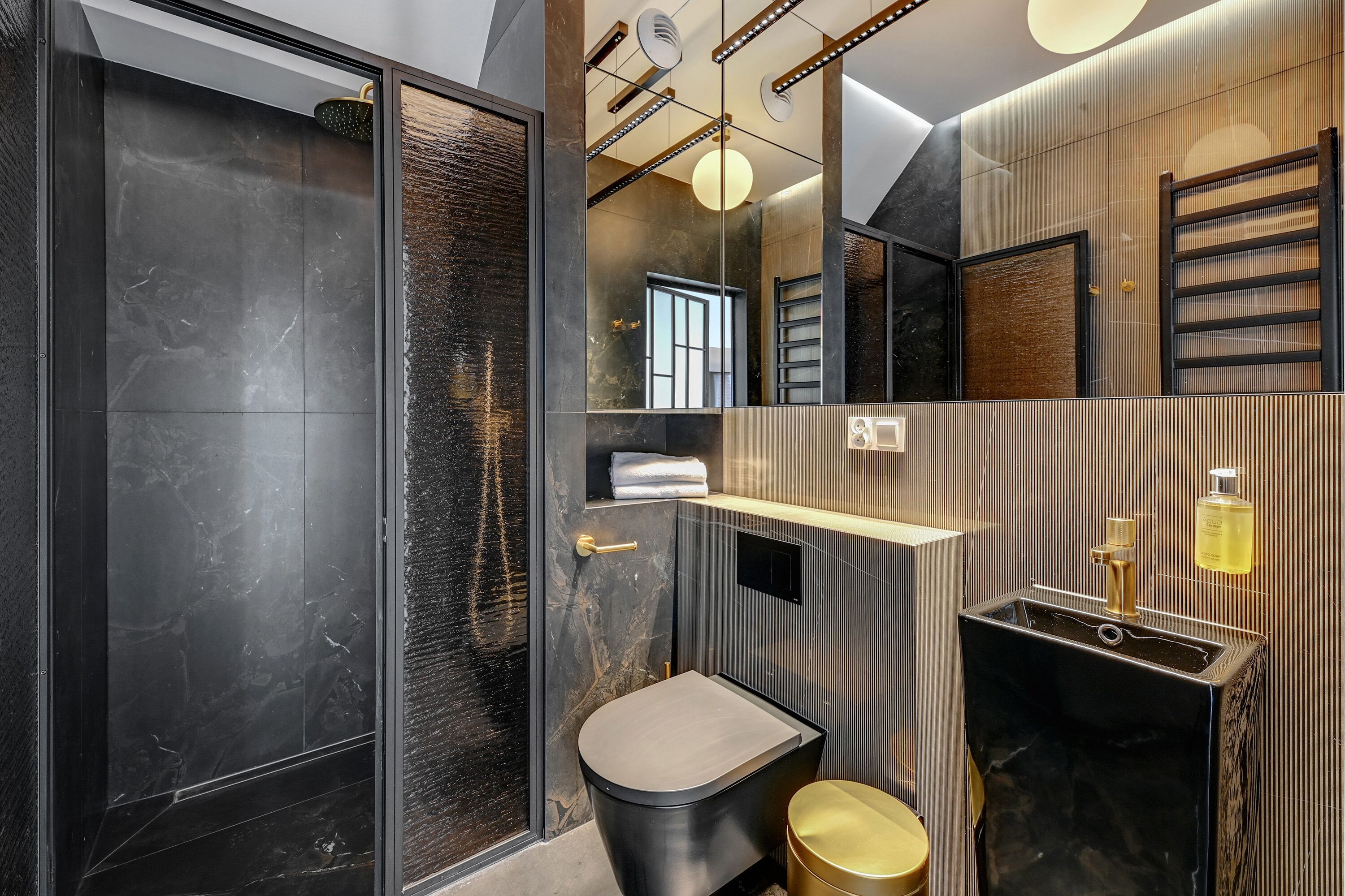 Et moderne badeværelse med et stort spejl, en sort vask og et toilet.