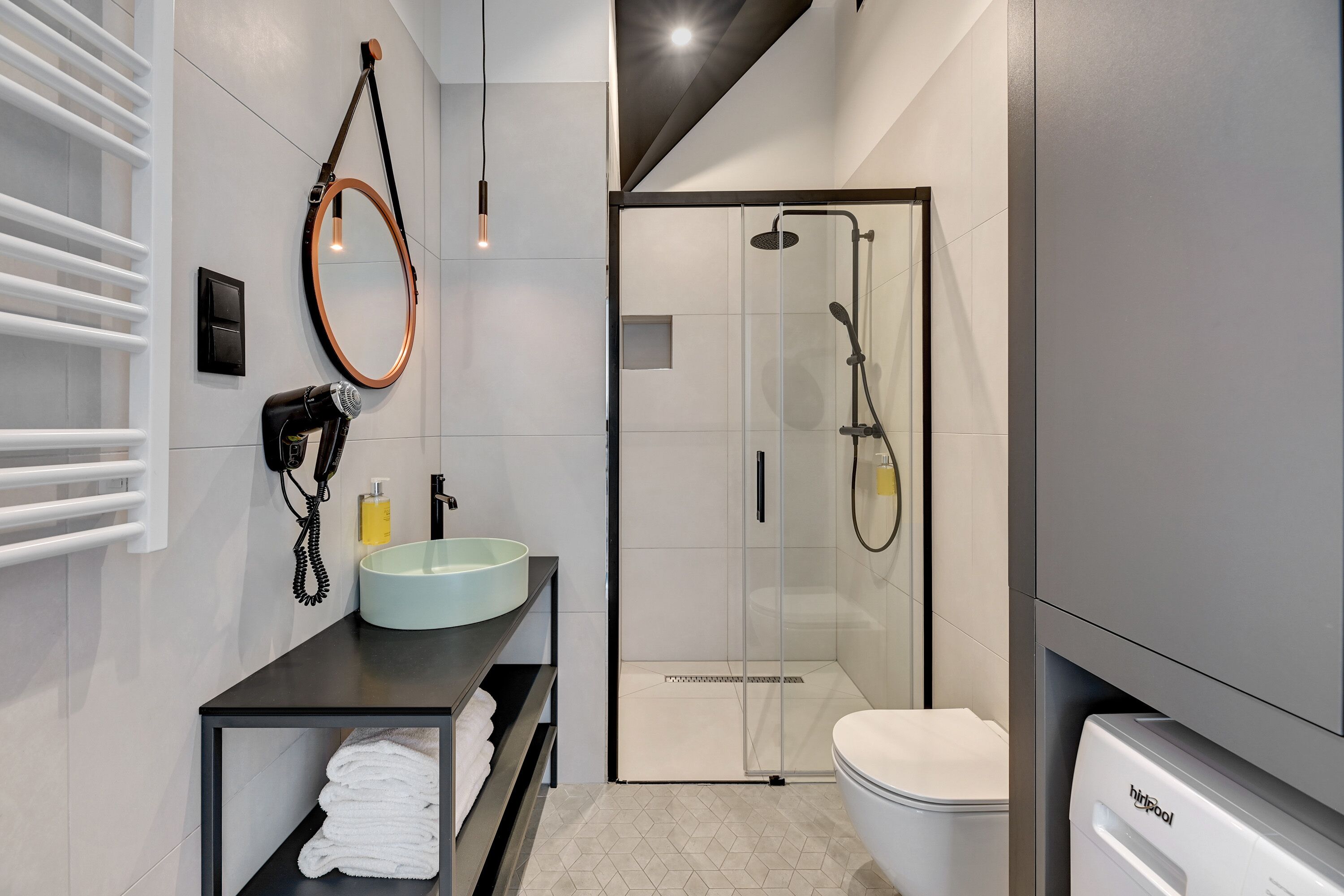 Un baño moderno con ducha envuelta en vidrio, un espejo redondo, un lavabo de tono claro y un inodoro.