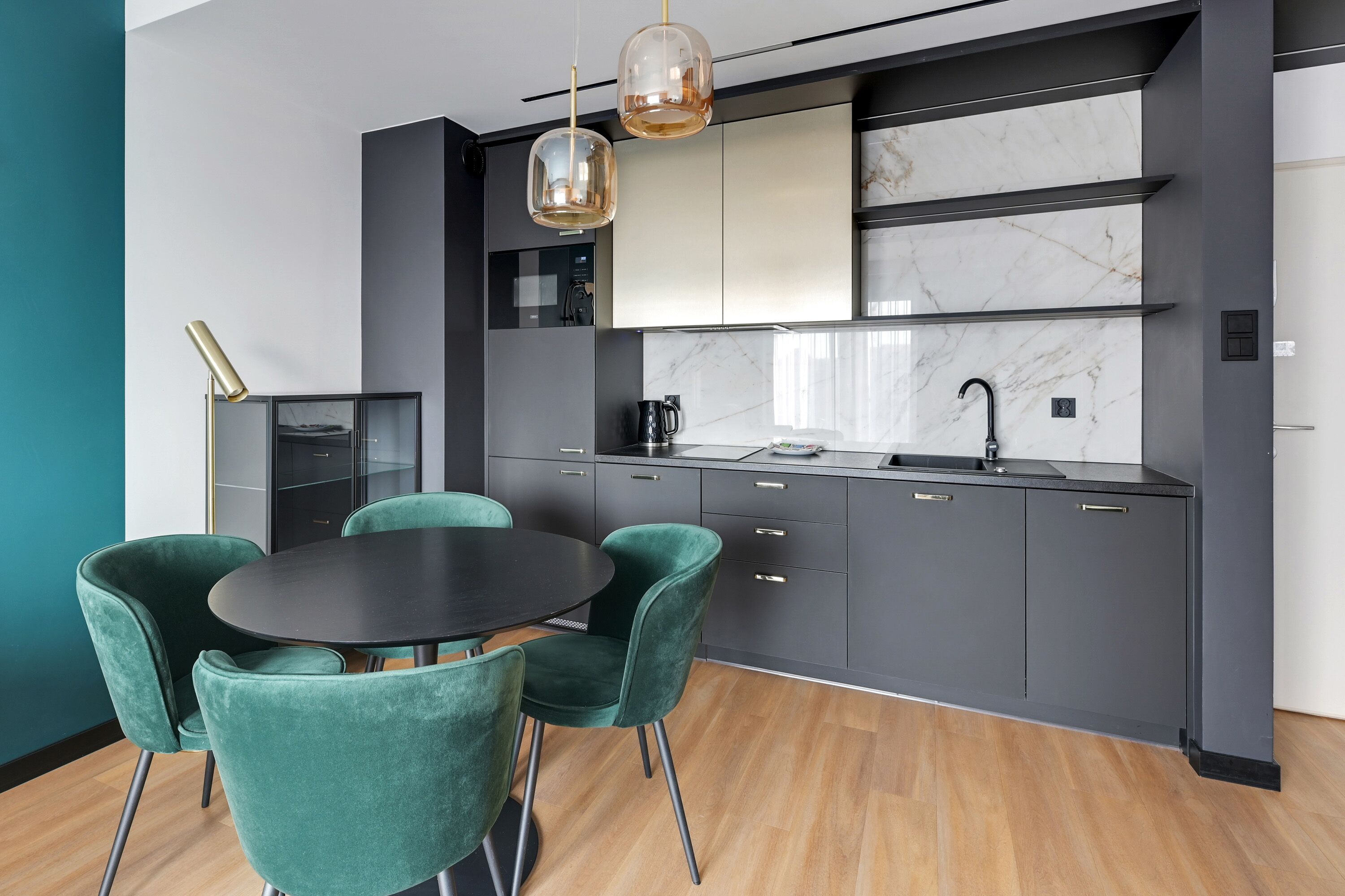 Una cocina moderna con una mesa redonda y sillas color turquesa, encimera negra y salpicadero de mármol.