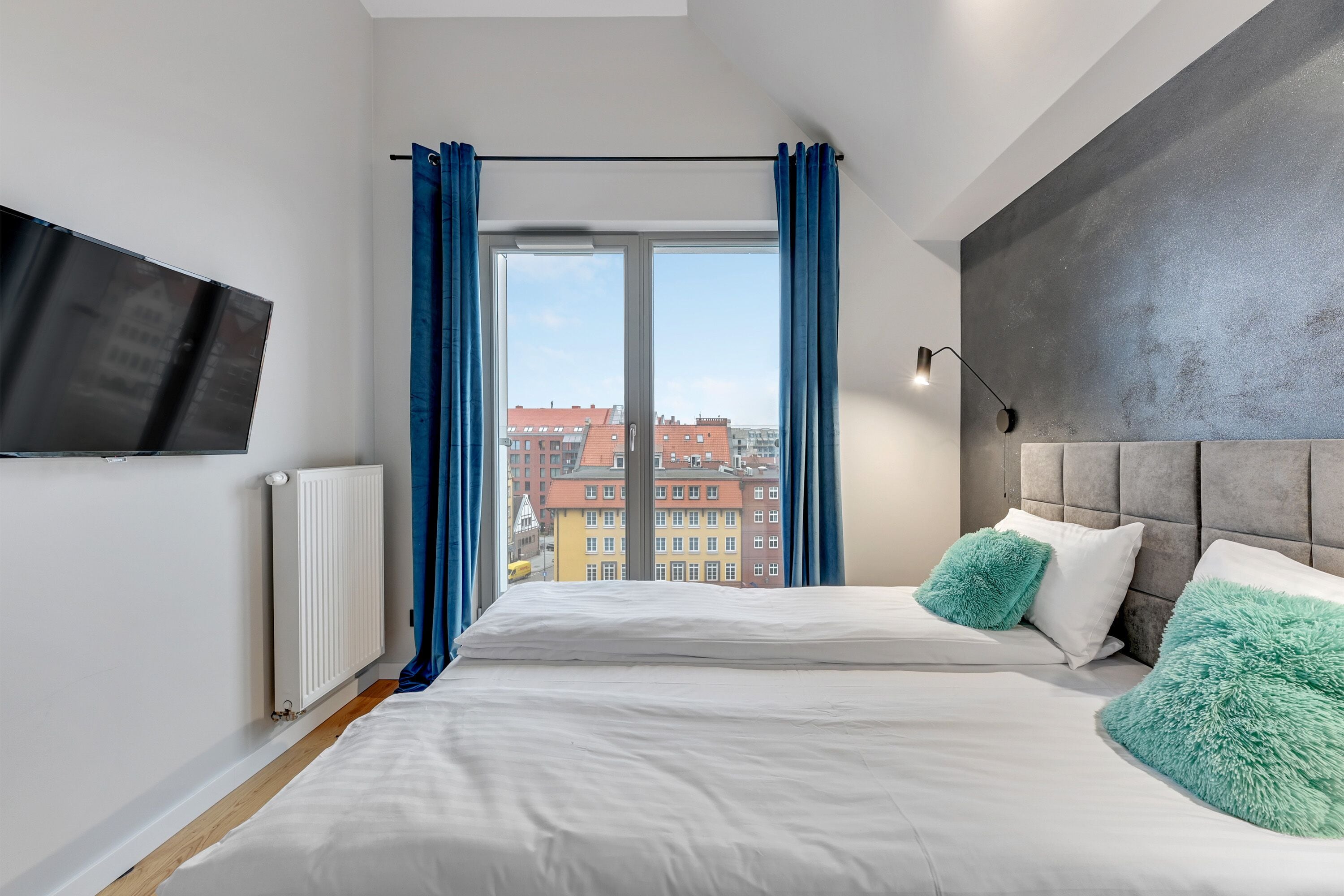 A modern bedroom with a large bed, a flat-screen TV, and a city view.