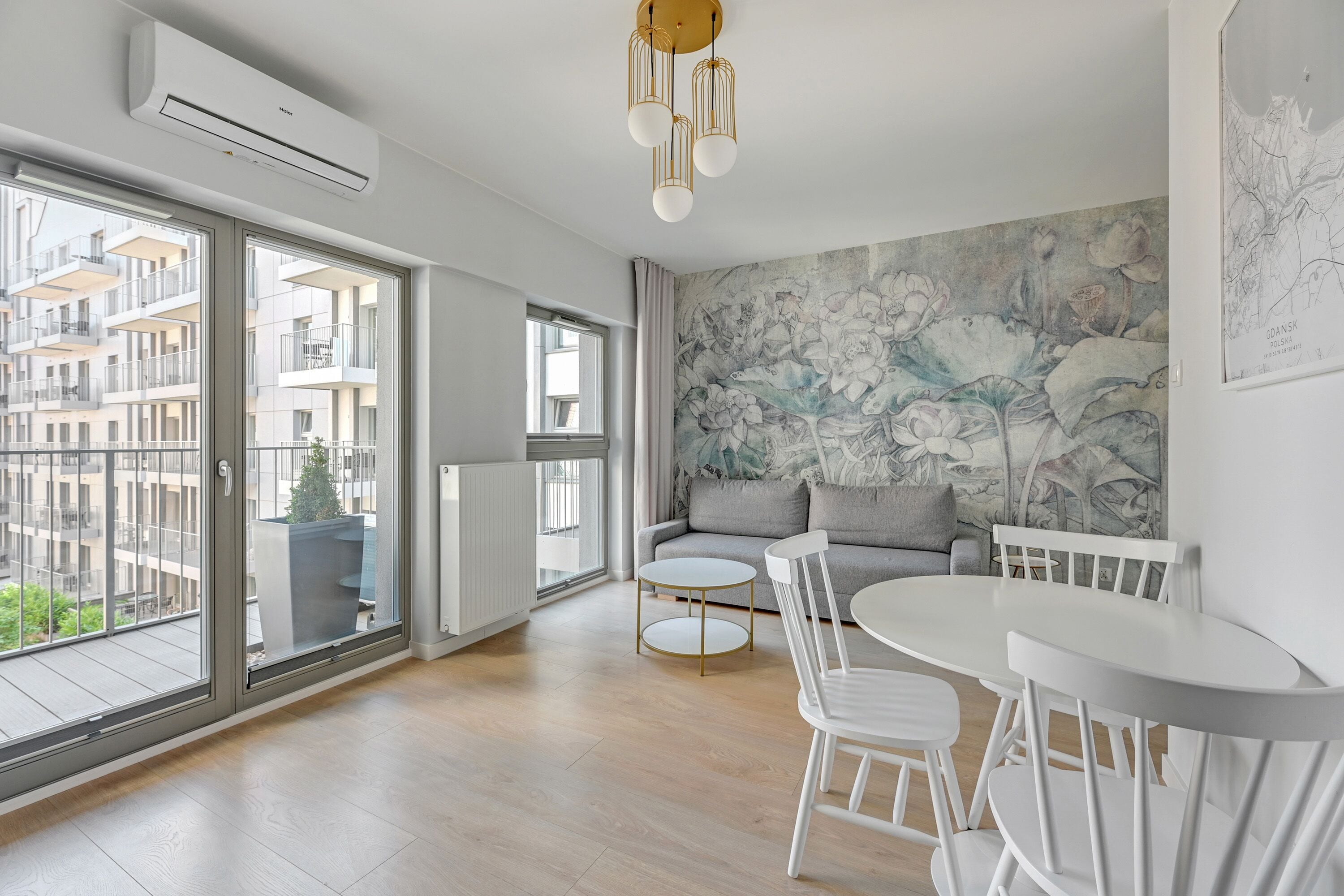 Una sala de estar moderna con un ventanal grande, un sofá gris, una mesa de comedor blanca con sillas, y un aire acondicionado instalado en la pared.
