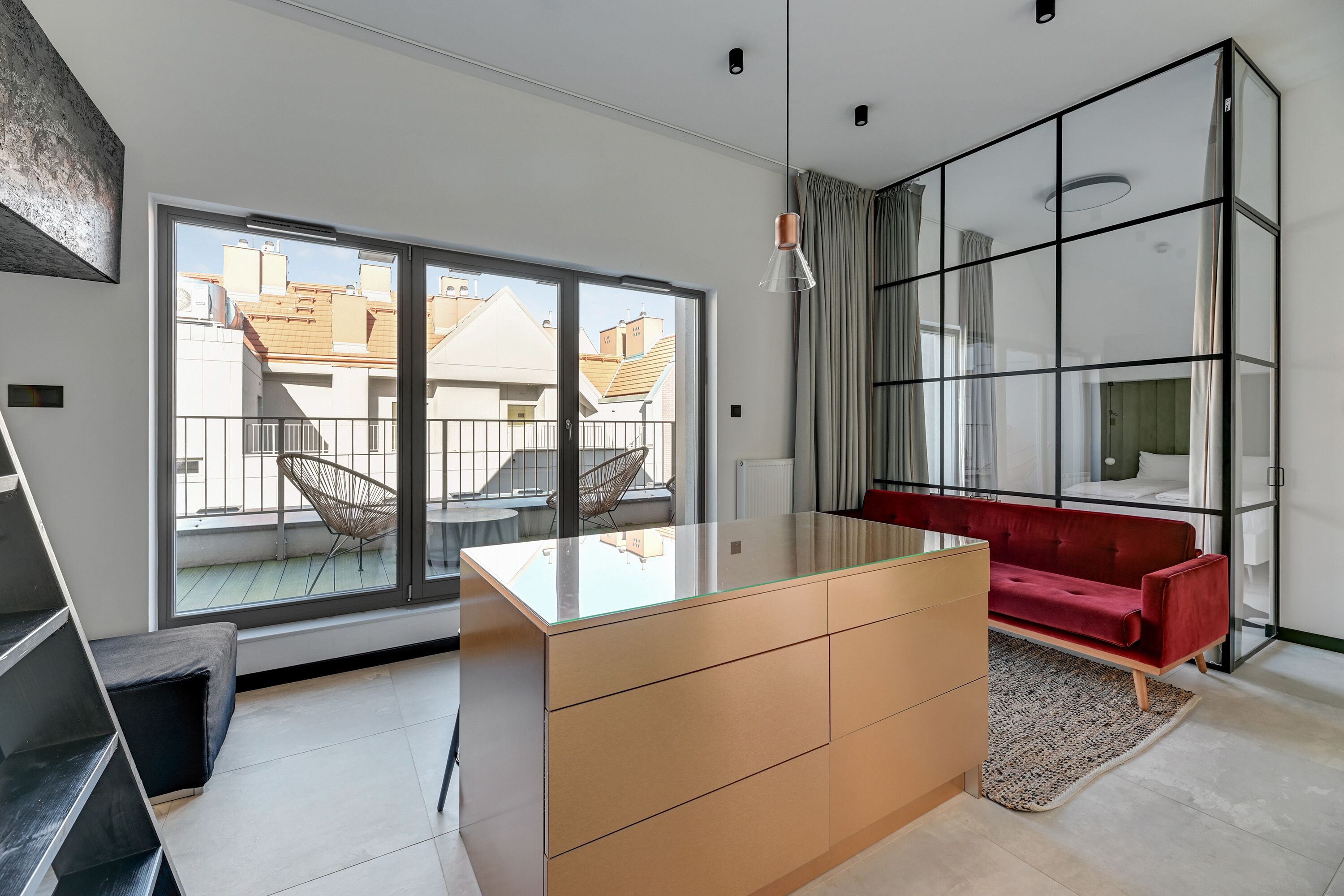 Una sala moderna con una isla de vidrio, un sofá rojo y un amplio ventanal corredero al exterior.