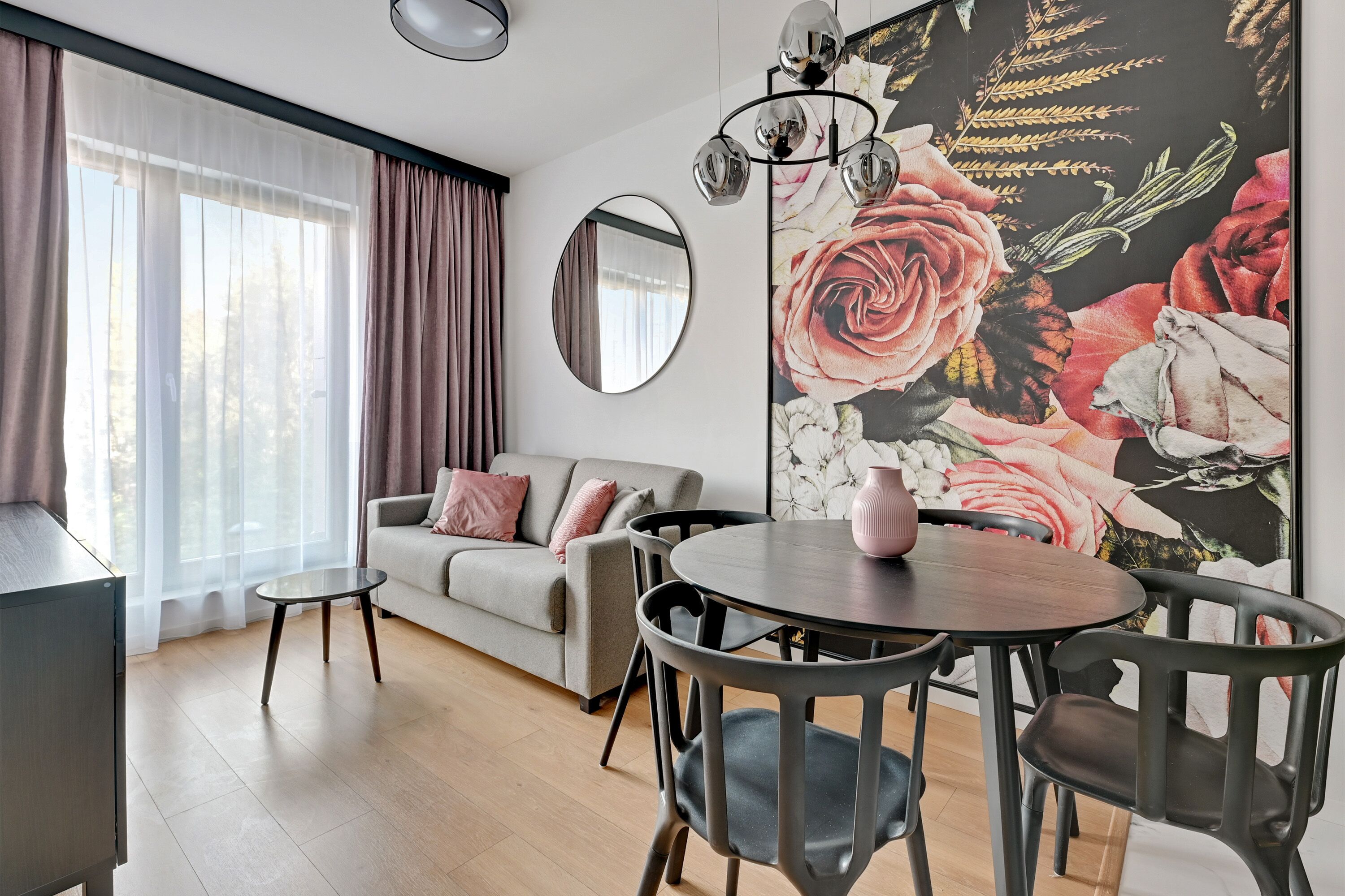 Una sala moderna con un sofá, una mesa de comedor con sillas, una mesita auxiliar, un espejo grande y un mural floral.