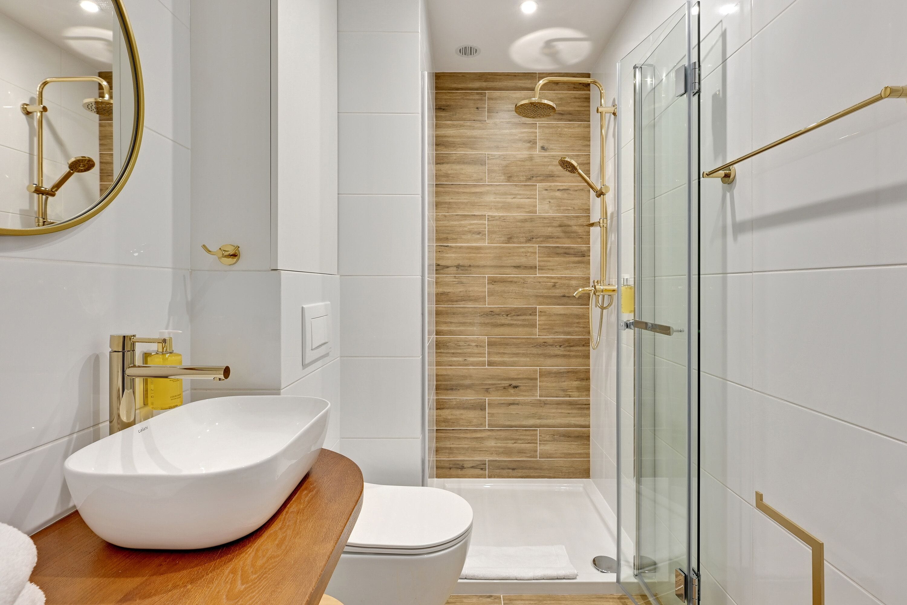 Et moderne badeværelse med en hvid vask, toilet og en bruseniche med glasvægge.