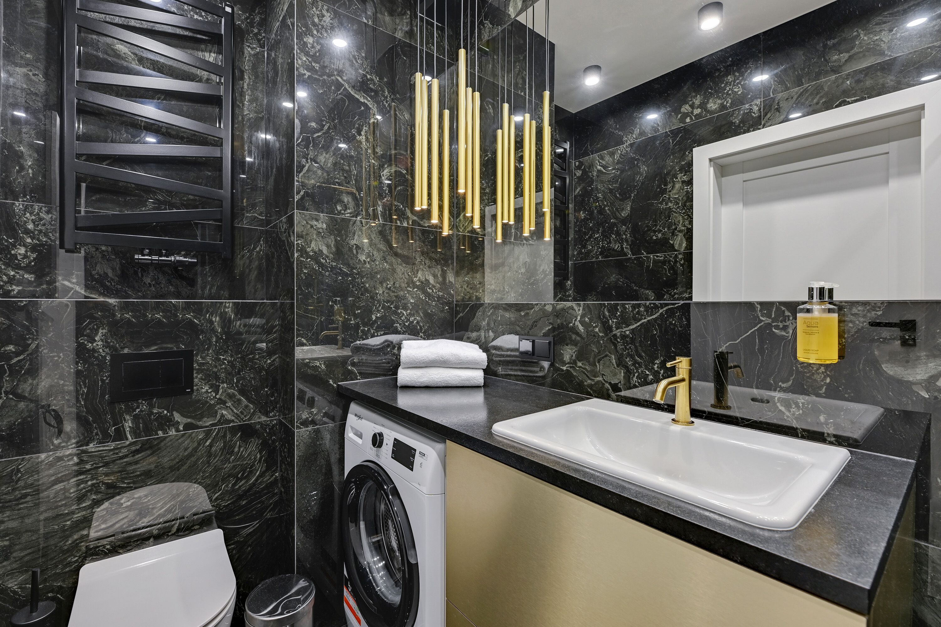 Ein modernes Badezimmer mit schwarzer Marmorwand, einem weißen Waschbecken, einem goldenen Wasserhahn und einem schwarzen und goldenen Handtuchhalter.