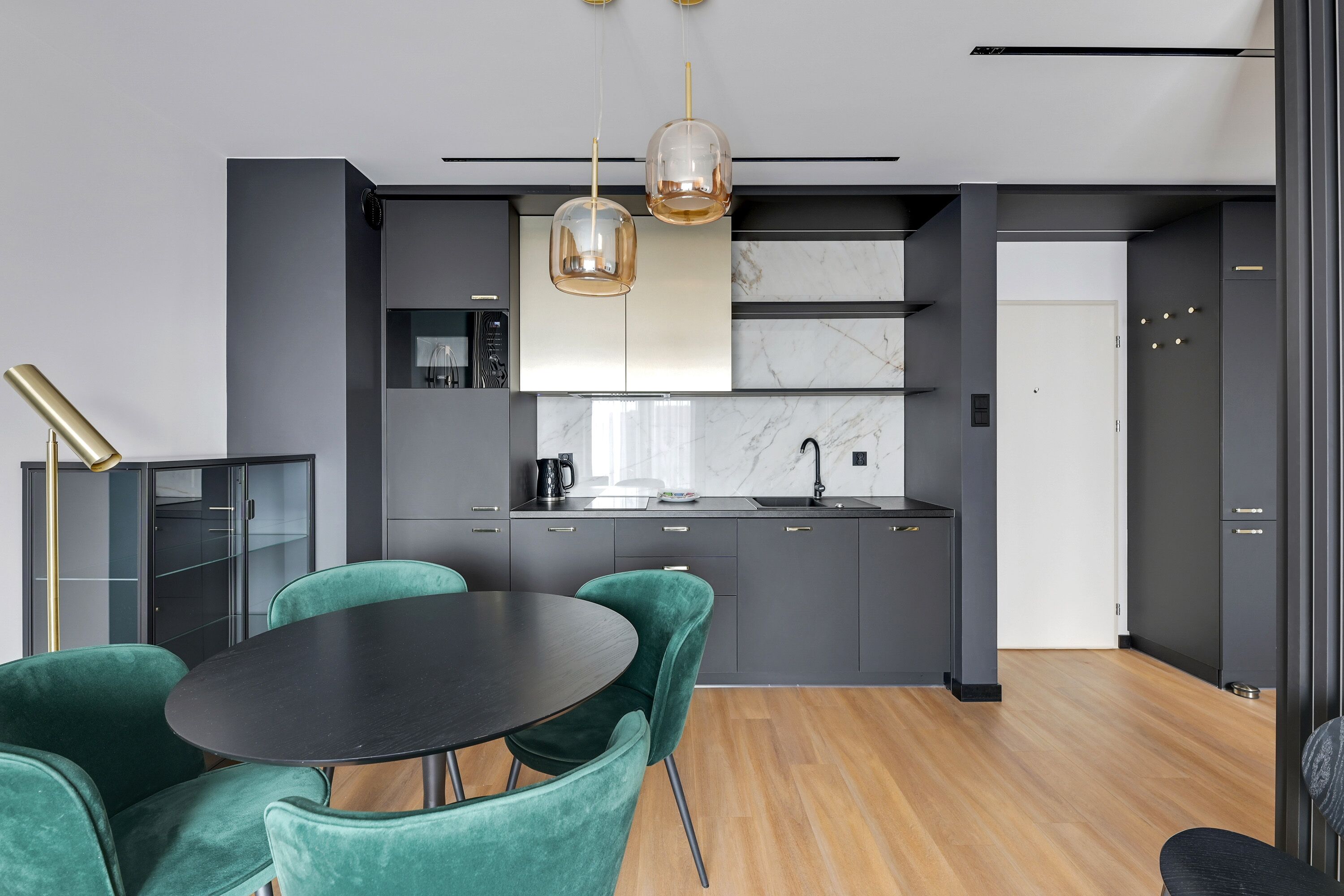 Una cocina moderna con armarios oscuros, salpicadero de mármol y encimera negra. Hay un comedor con una mesa redonda y sillas tapizadas en verde.