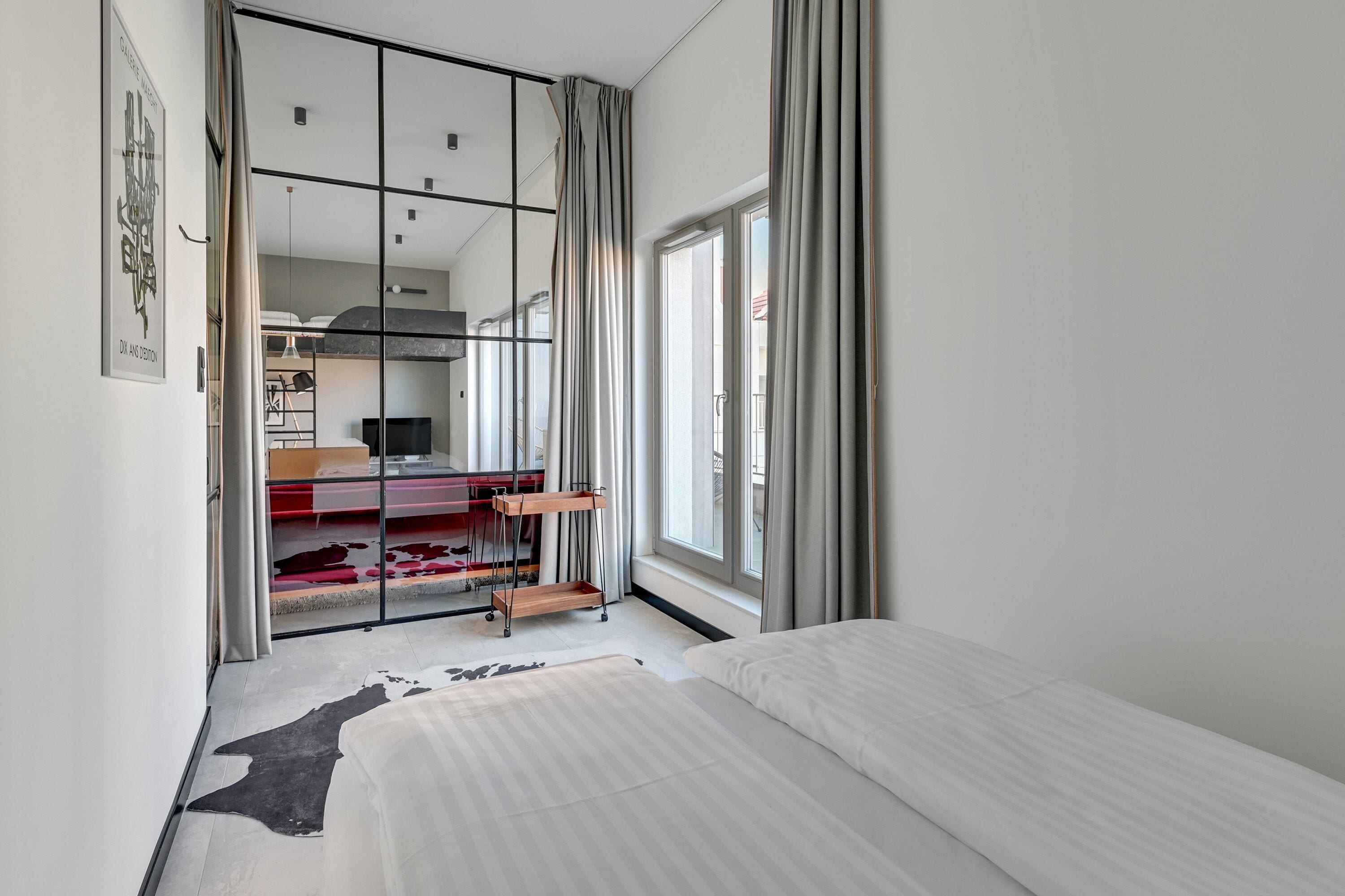 Habitación de hotel moderna con una cama grande, un separador de vidrio, un escritorio y vistas a la ciudad.