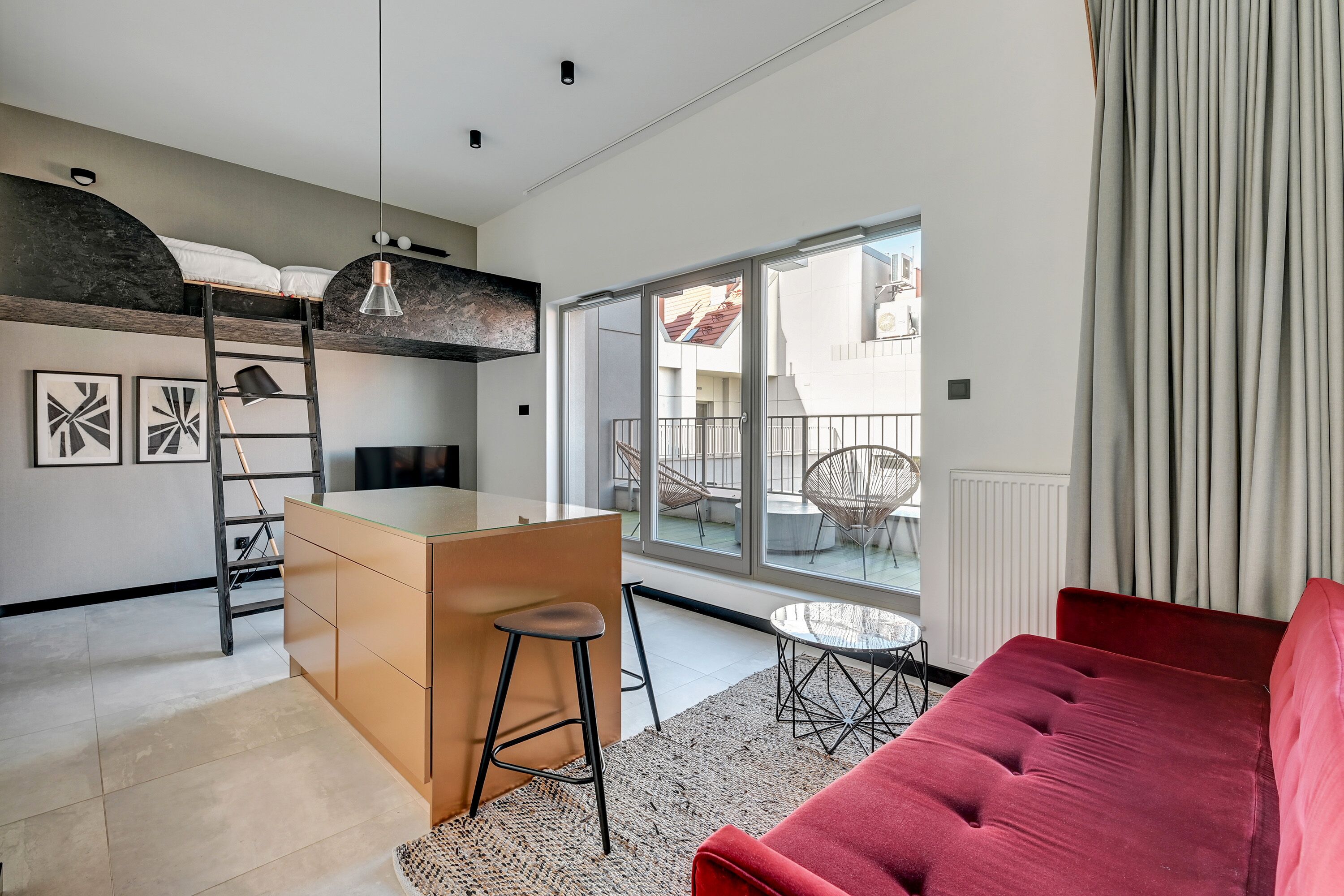 A modern apartment with a bunk bed, kitchenette, red sofa, and large windows offering a view of the outside.