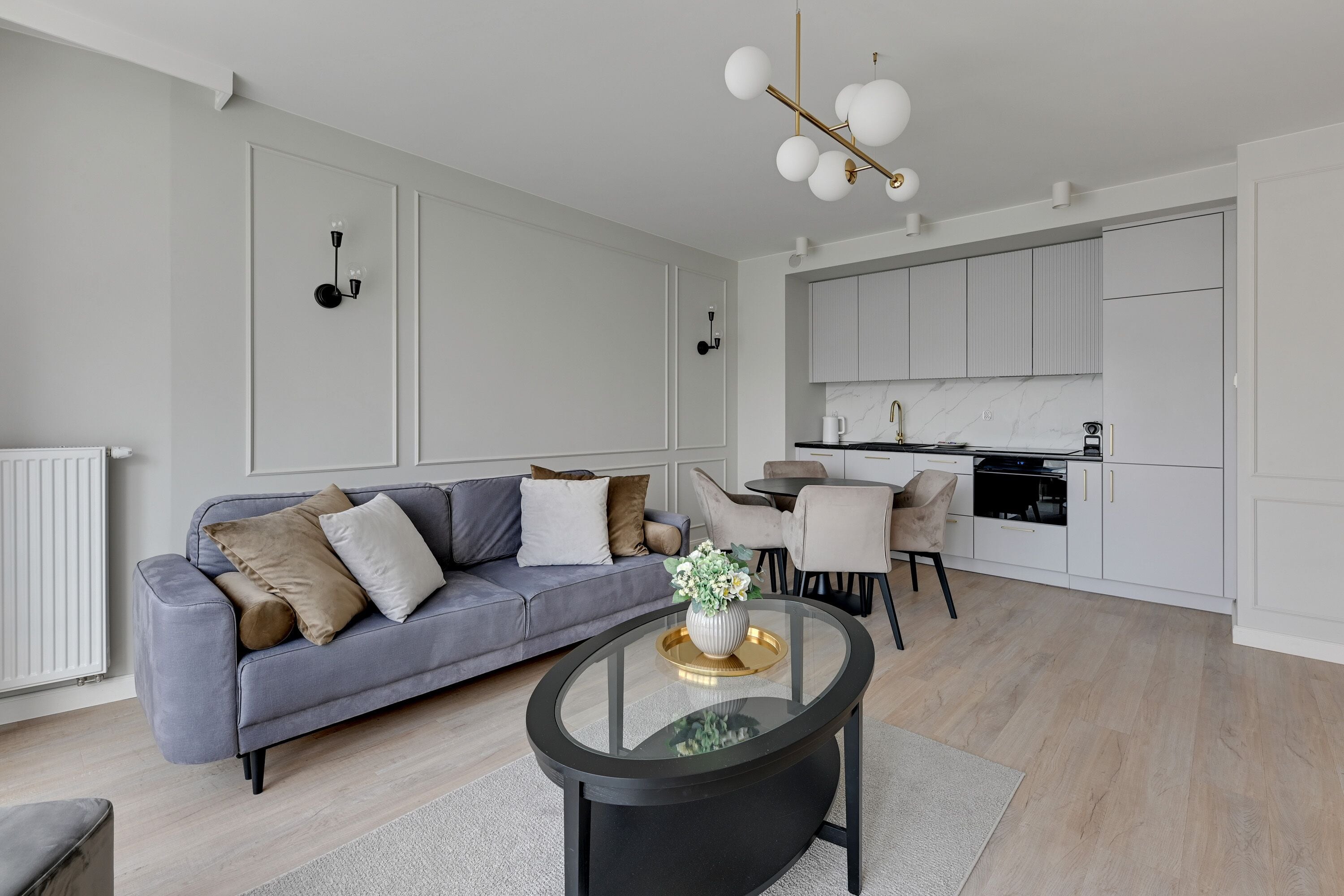 Una sala de estar moderna con un sofá gris, una mesa de centro de vidrio y una zona de comedor con una mesa y sillas blancas.