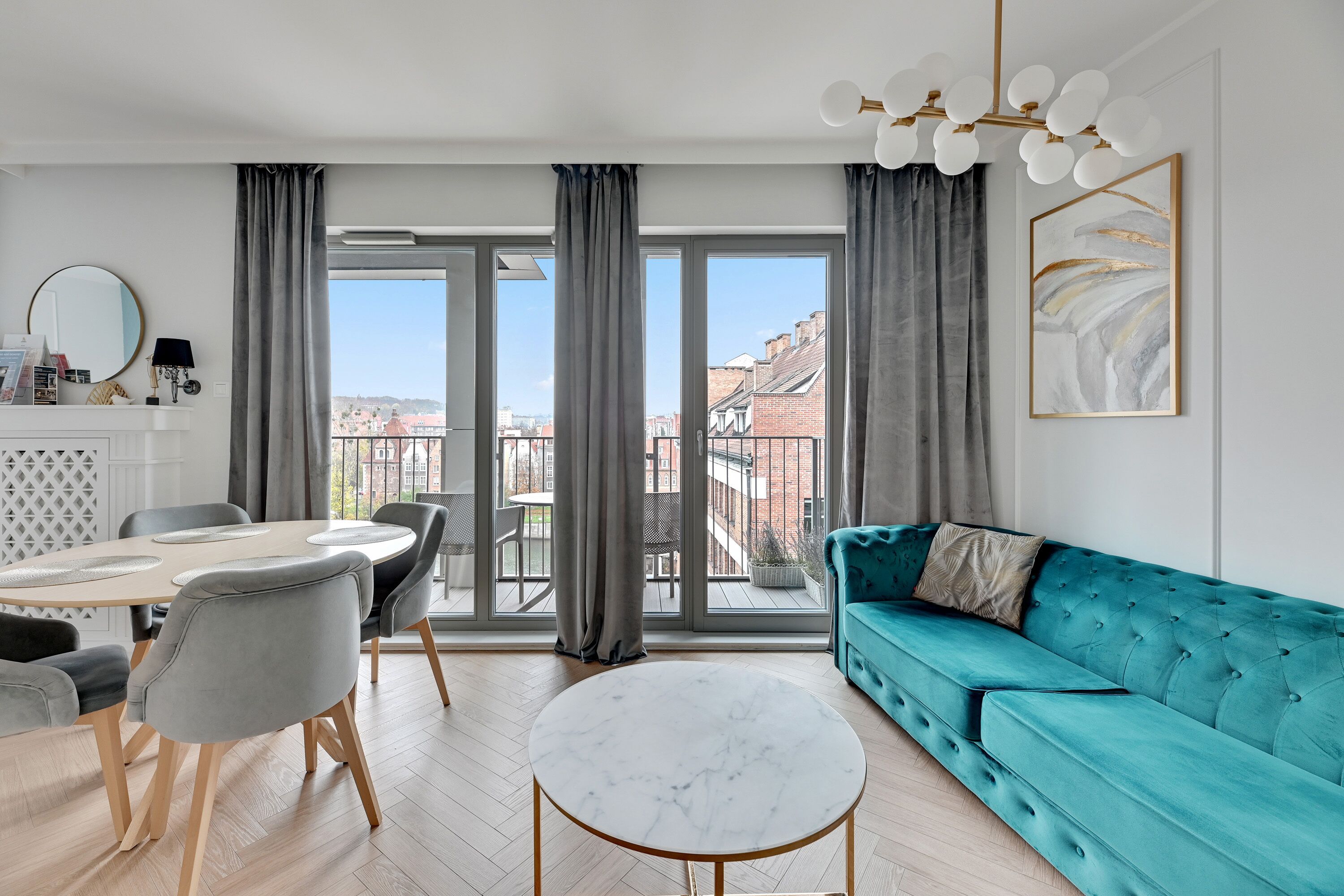 Un salon moderne avec un canapé de couleur turquoise, une table basse ronde en marbre et un coin repas comprenant une table blanche et des chaises grises.