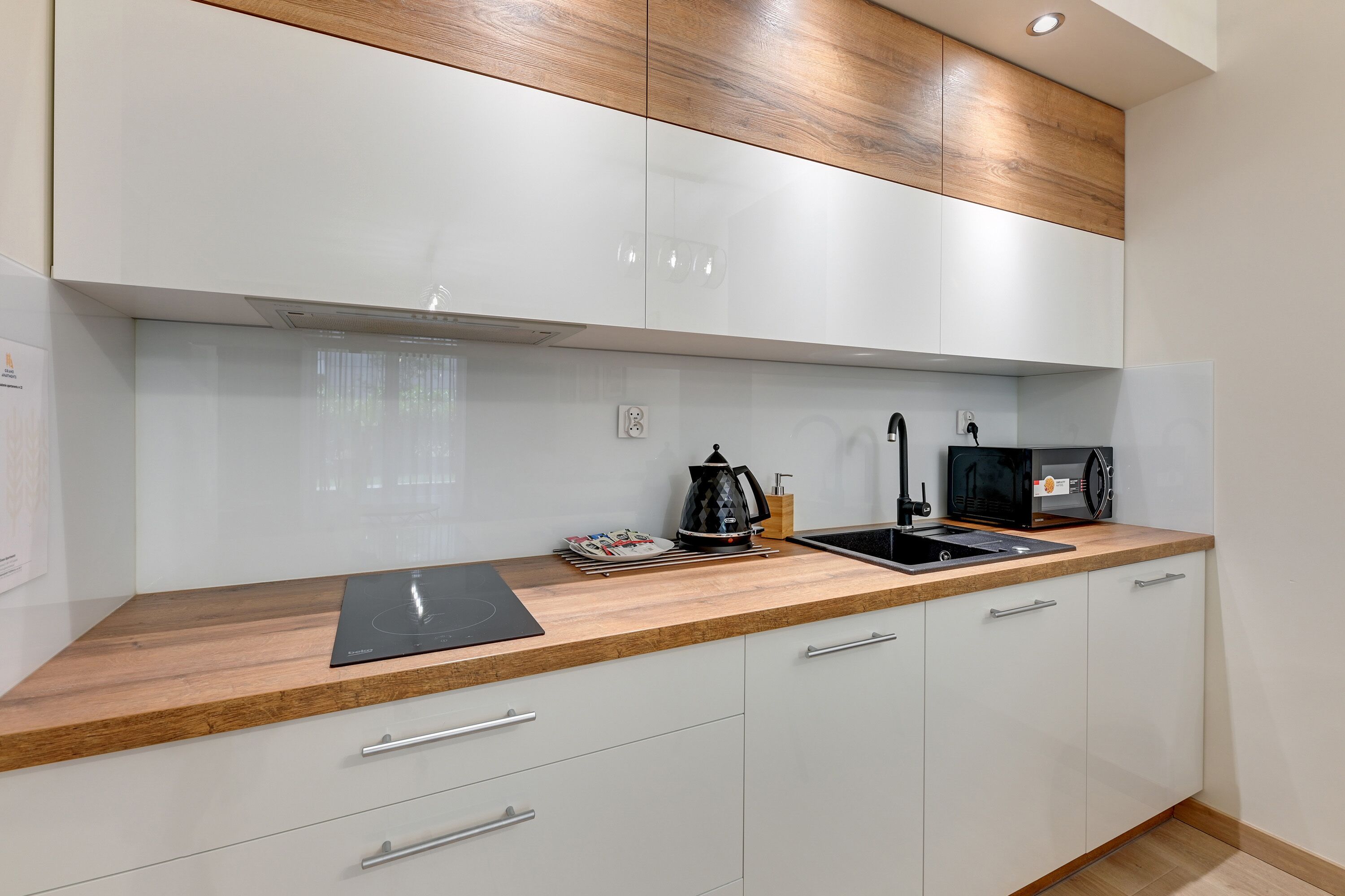 A modern kitchen with white cabinets, a wooden countertop, and a black induction cooktop.