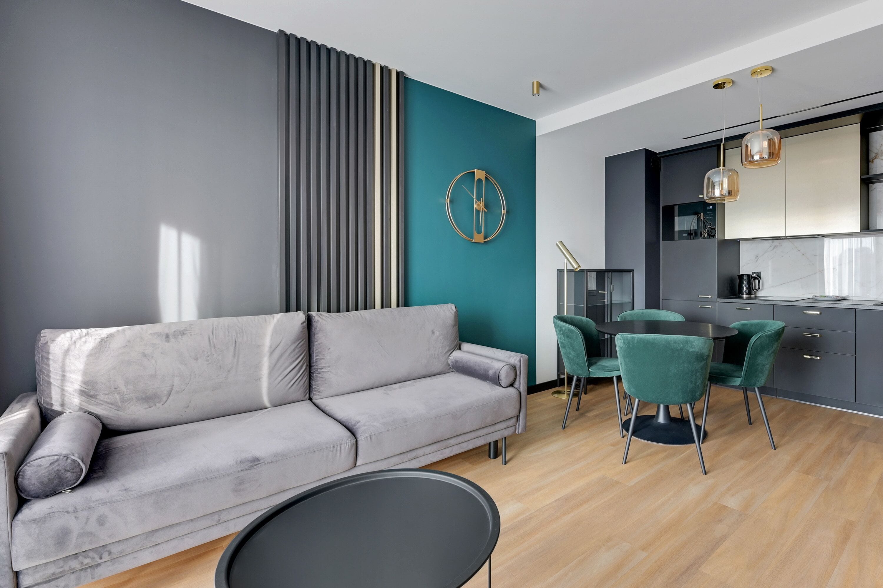 Un salon moderne avec un canapé gris, un mur d’accent de couleur turquoise et un coin repas avec des chaises vertes.
