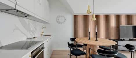 A modern kitchen with a wooden dining table, black chairs, and a TV in the background.