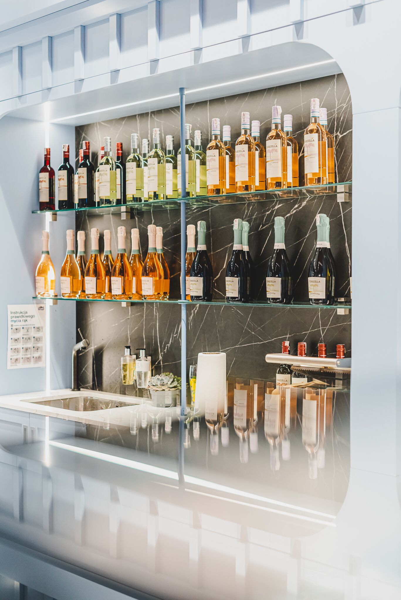 A bar area with shelves of various bottles, a marble backsplash, and a reflective surface.