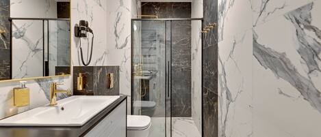 A modern bathroom with a marble floor and walls, a large mirror, a sink with a gold faucet, and a glass-enclosed shower.