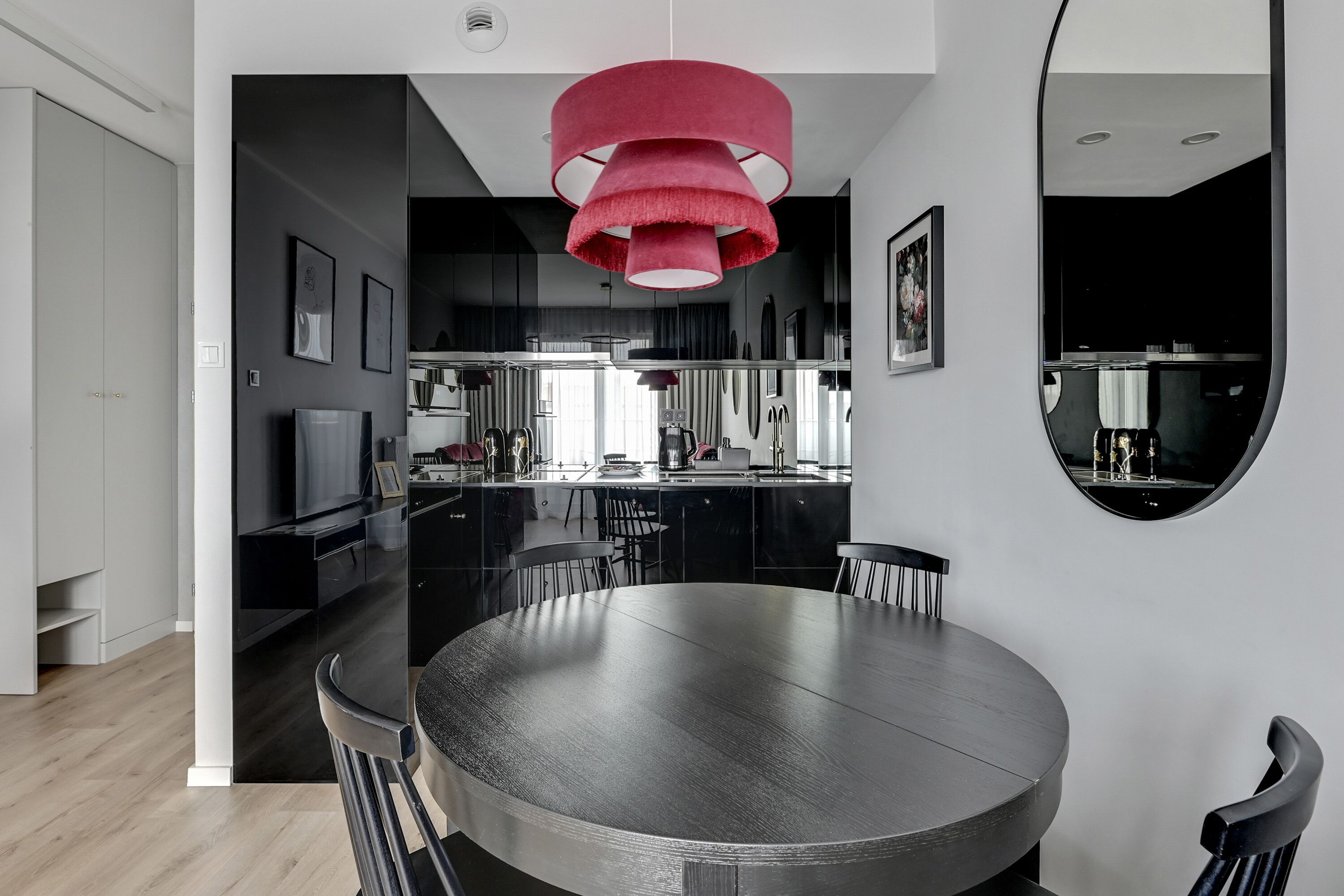 Un espace repas moderne avec une table ronde et des chaises, un luminaire suspendu rouge et une cuisine en arrière-plan.