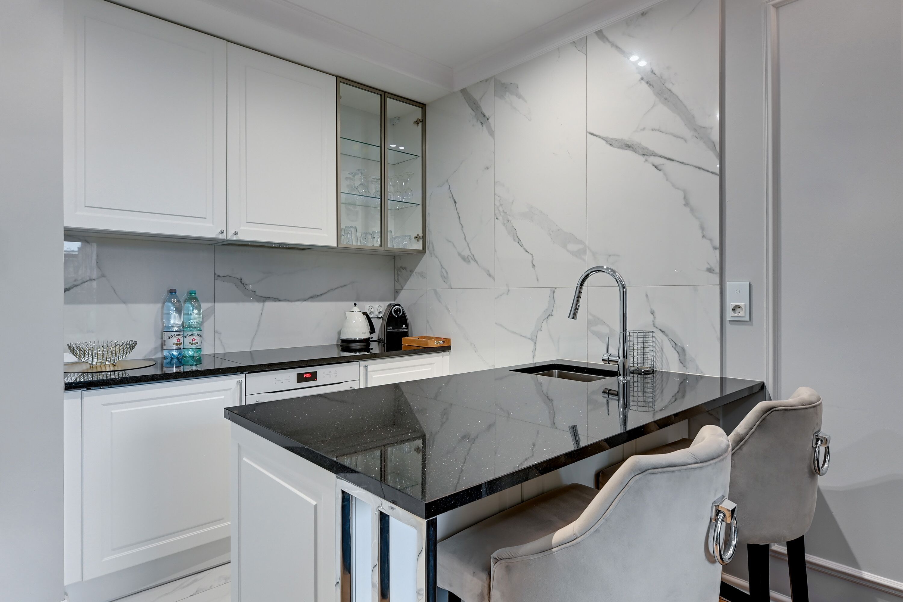 A modern kitchen with marble backsplash, white cabinetry, and a black countertop.