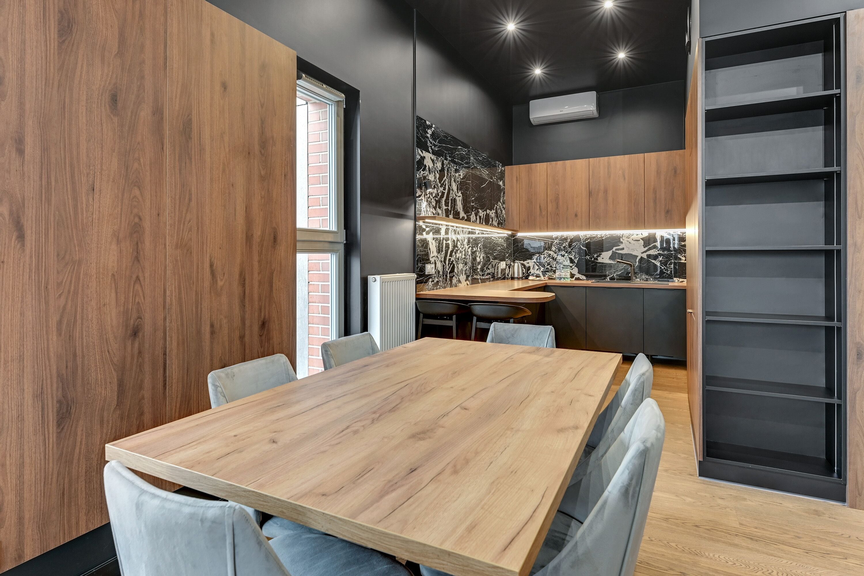 A modern kitchen with a wooden table and chairs, a black backsplash, and a built-in shelving unit.