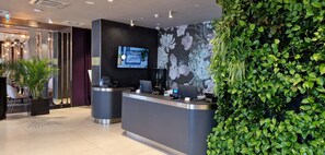 A reception area with a modern design, featuring a reception desk, a mounted TV, and a wall with a floral pattern. - Grano Apartments Gdańsk Residence (Gdansk)