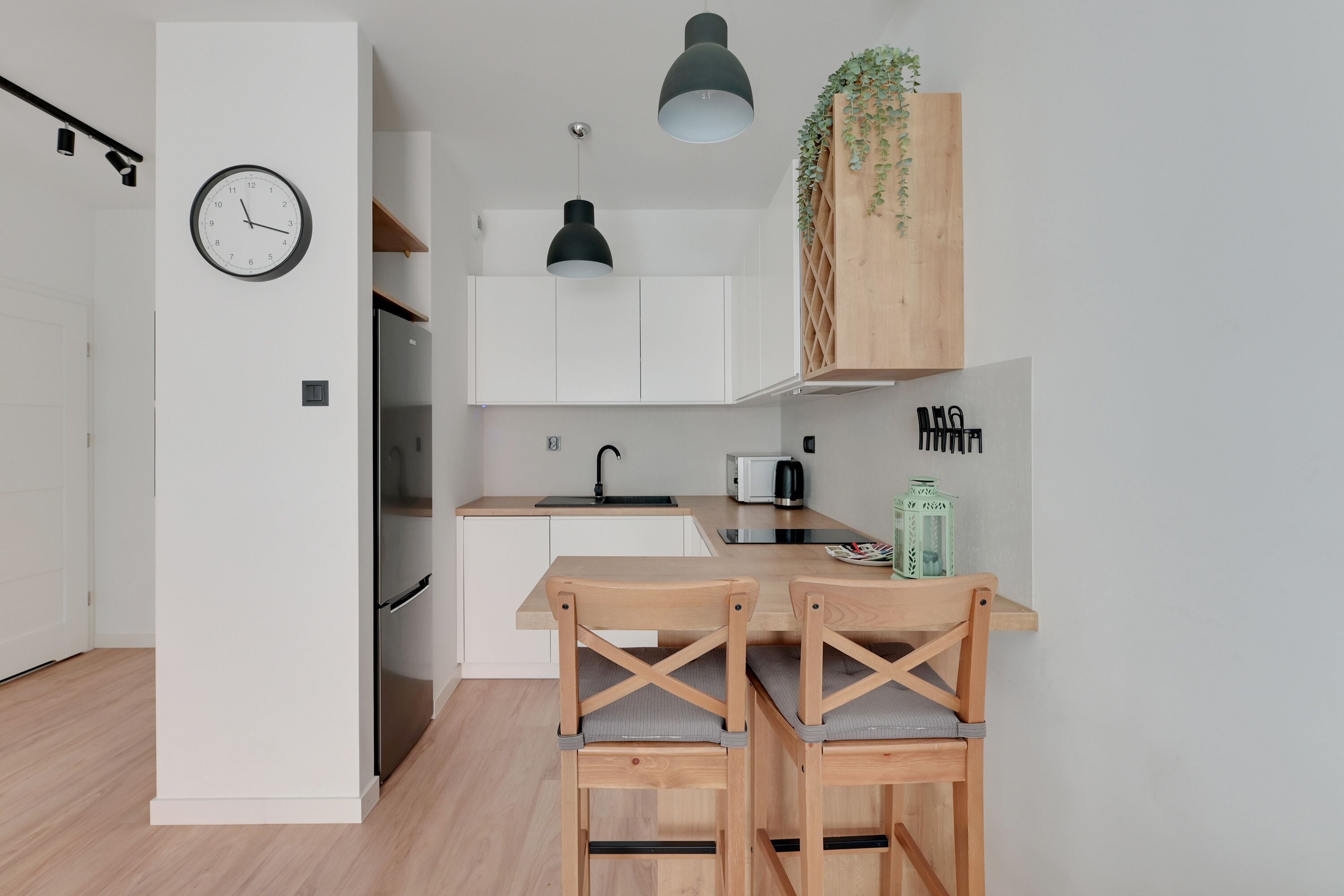 A modern kitchen with white cabinets, a black pendant light, and a wooden bar area with two chairs.