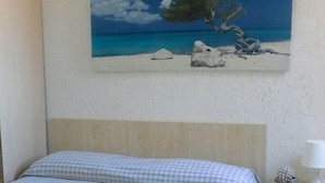 A bedroom with a bed, a nightstand, a painting of a beach scene, and a blue and white checkered bedspread.