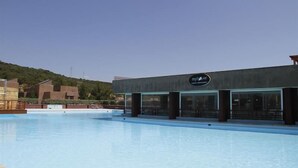 A modern hotel with a pool area, a sign reading "my hotel ve", and a view of a hilly landscape in the background.