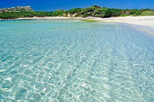 Una playa despejada con aguas poco profundas, orilla de arena y un promontorio rocoso al fondo.
